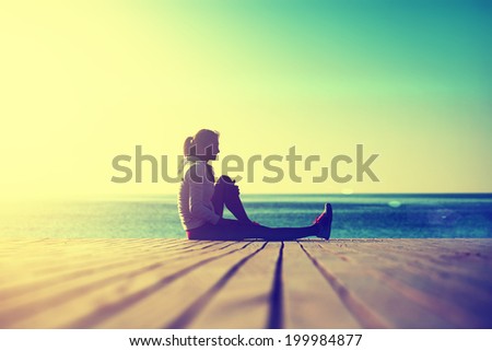 Sunny morning on the beach, athletic woman resting after stretching exercise at the morning training on the beach