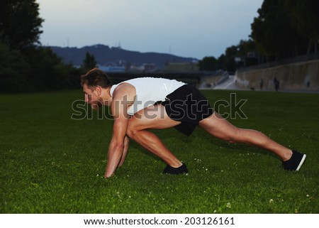 Young muscular sportsmen in white t-shirt ready to start standing on the grass, athletic runner at evening jog in the park, health lifestyle and fitness concept