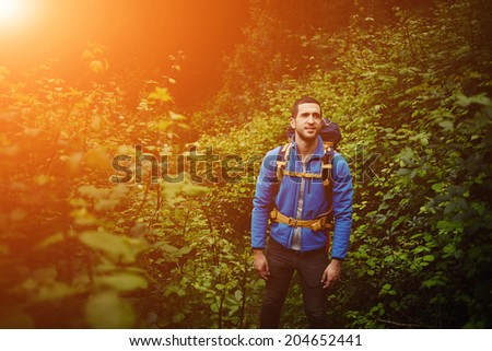 Beautiful man with rucksack resting after long way standing in the forest, adventure and extreme sport