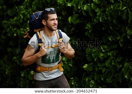 Beautiful man with rucksack resting after long way standing in the forest, adventure and extreme sport