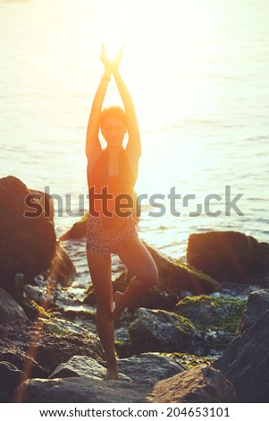 Silhouette of a slim girl with beautiful figure doing yoga on the sea with sunrise, spiritual meditation and relax