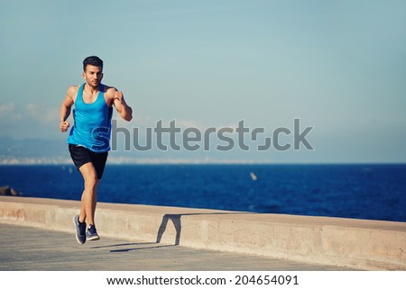 Male jogger with high speed running along the sea on the pier, athletic sportsman on the evening run, fitness and healthy lifestyle concept