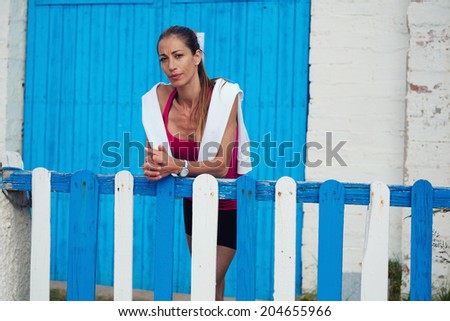 Beautiful middle age woman with good figure resting after run leaning one\'s elbows beautiful wooden fence, fitness and healthy lifestyle concept