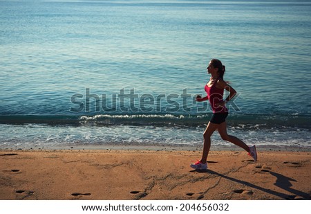 Beautiful female jogger with strong figure run on sand, athletic female jogger running on the beach, fitness and healthy lifestyle concept