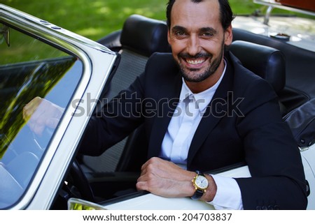 Rich confident handsome businessman sitting in the cabriolet classic car and smiling at camera, lifestyle and successful business concept