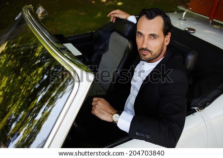 Rich confident businessman with gold wrist watch in the hand sitting in the cabriolet classic car and looking at camera, lifestyle and successful business concept