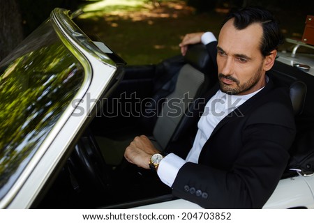 With reflective glance stylish rich man seated in his cabriolet classic car looking away, lifestyle and successful business concept