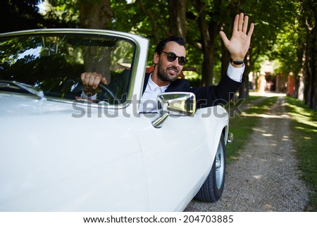 Rich stylish and elegance man in sunglasses drive his luxury cabriolet car and greeted to someone smiling, lifestyle and successful business concept