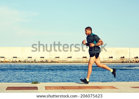Attractive african american sportsman running in the sea port, male runner in action jogging along the sea, fitness and healthy lifestyle concept