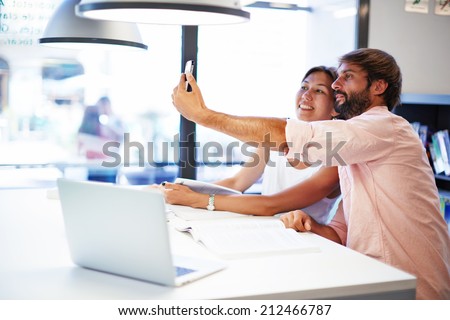Two colleagues friends taking the picture to them self sitting in the office, man and woman taking selfie with telephone camera, working funny in the office, happy people taking picture smiling