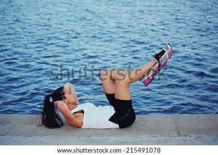 Athletic woman doing sports outdoors, sporty brunette with beautiful figure doing workout lying down,athletic girl with muscular body doing exercise on the sea background,fitness and healthy lifestyle