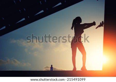 Young female runner silhouette against the sunset, silhouette of female jogger doing stretching exercise on beautiful sunset background with clouds, women doing workout on sunset sky background