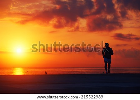 Male runner with athletic figure running alone at orange sunrise on the beach, fitness training on the beach, beautiful runner silhouette in action, fitness and healthy lifestyle