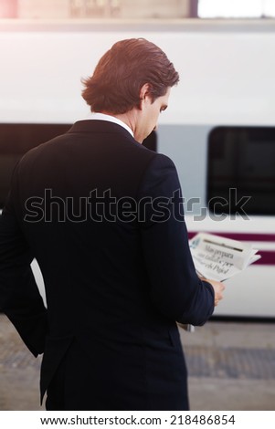 Rich man in suit reading newspaper on the way to work, businessman waiting to the train in railway station and reading news, handsome businessman holding newspaper in the hands standing in platform