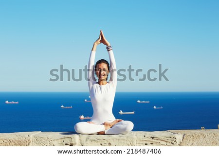 Young healthy woman at sunny day practicing yoga at high altitude on beautiful sea background, happy attractive woman engage yoga at sunny day in summer outdoors, feeling healthy