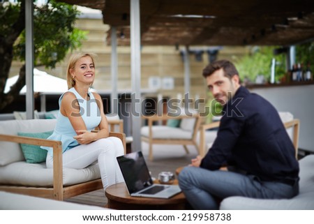 Young businessman discussing plan with female colleague, businesspeople working with laptop sitting in modern place, business meeting of two colleagues outside the office, business and success concept