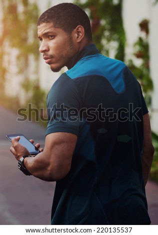 Handsome sportsman holding mobile phone and looking away, muscular build dark skin runner resting after run using his mobile phone, attractive muscular runner taking break,  using technology concept