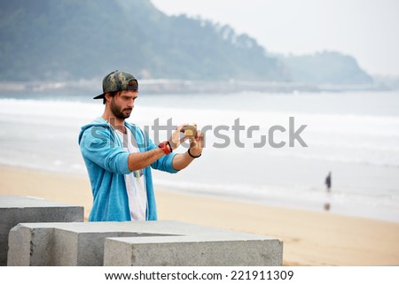 Beautiful hipster standing on the ocean beach enjoying the view, young attractive hipster man taking a picture of beautiful beach view with mobile telephone, young man take photo on holidays vacation