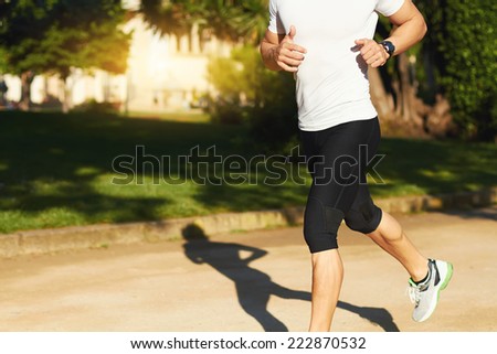 Athletic sportsman with strong muscular body jogging outdoors, crop of body, sunny summer day in beautiful green park, running man in action, shadow of jogger running, be in form with sport outdoors