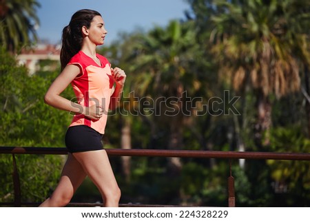 Attractive young woman running fast in beautiful park, perfect sunny day for fitness sport outdoors, brunette female runner jogging in palm trees park at sunny morning, fitness sport concept