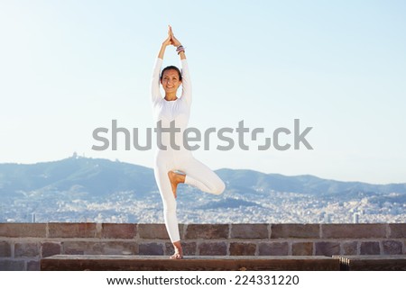 Beautiful yoga with amazing view of city on background, pretty healthy woman with perfect body stand in one of yoga pose and looking to the camera with smile, feeling neatly with yoga