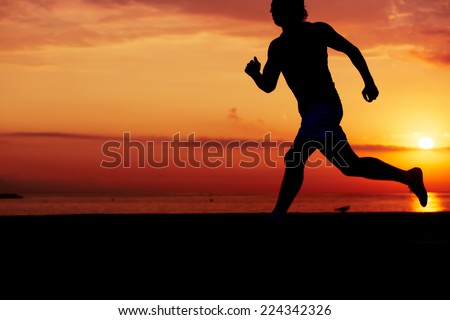 Silhouette of athletic runner jogging on the beach against orange sunrise, male jogger with muscular body in action, sportsman running with the speed, fitness and healthy lifestyle concept