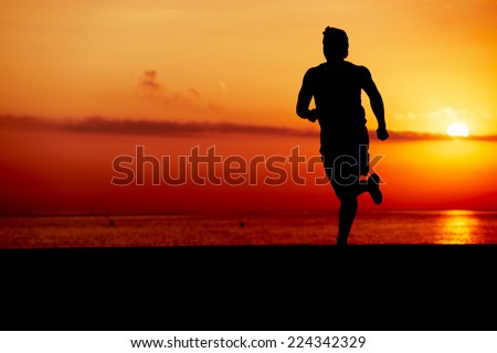 Silhouette of fit man jogging on the beach against orange sunrise, male jogger with muscular body in action, sportsman running with the speed, fitness and healthy lifestyle concept