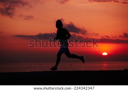 Silhouette of male runner in action, attractive jogger at morning training on the beach, man running into colorful sunset on the beach, fitness and healthy lifestyle concept
