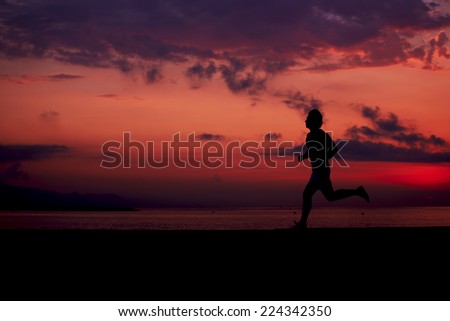 Silhouette of athletic runner jogging on the beach against orange sunrise, male runner with muscular body at morning jog, attractive jogger in action, fitness and healthy lifestyle concept
