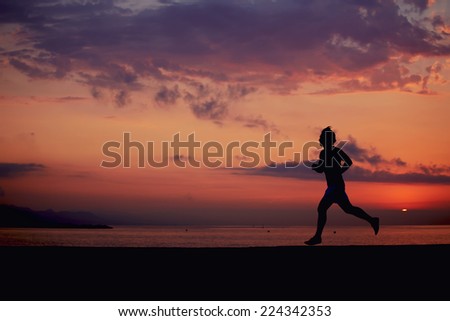 Silhouette of male runner jogging on the beach against orange sunrise, male jogger with muscular body in action, sportsman running with the speed, fitness and healthy lifestyle concept