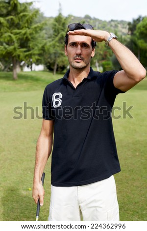 Professional golf player observe direction of ball standing on golf course at sunny day, handsome wealthy man in polo t-shirt standing on golf course holding driver in the hand