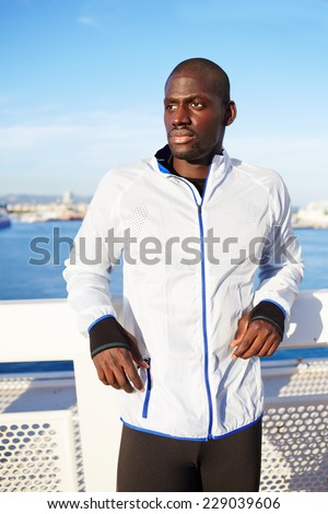 Portrait of sportsman in white wind breaker taking break standing on sea background, black fit man resting after workout outdoors, soft evening light, tired to run jogger resting