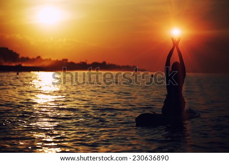 Silhouette of beautiful woman holding sun in the hands during sup yoga meditation,yoga training in harmony with nature, silhouette of paddle board yoga performed by beautiful woman, spiritual concept