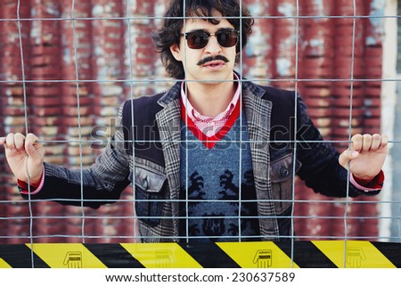 Handsome brunette hipster man in glasses standing opposite barrier fence
