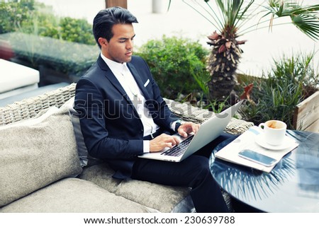 Confident man in suit typing on laptop computer keyboard, businessman seated in cafe working with computer, businesspeople using modern devises, rich businessman working with laptop computer in cafe