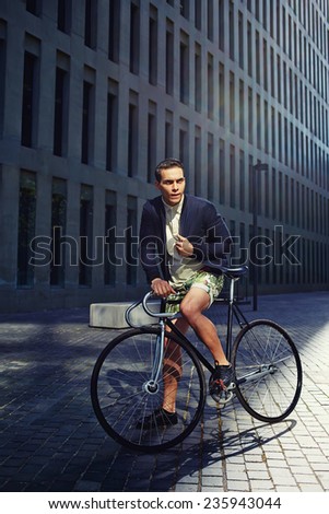 Attractive young man ready to ride on fixed gear bicycle looking away, stylish hipster man riding on fixed gear bike, young handsome man standing with the bicycle in modern city zone