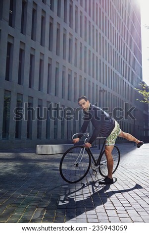 Stylish hipster man riding on fixed gear bike, young handsome man standing with the bicycle in modern city zone, attractive young man ready to ride on fixed gear bicycle looking away