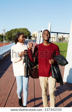 Full length of cheerful university students walking on campus, young stylish students walking during the break, friends having a great time together, two college friends laughing having good time