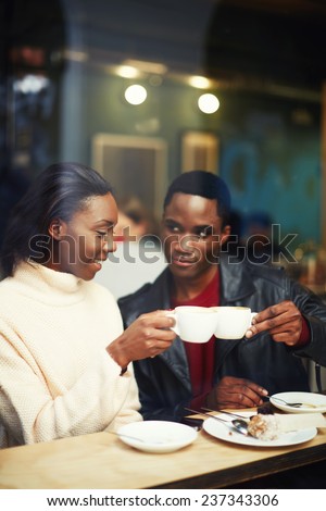 Happy stylish friends having coffee together, laughing young couple in cafe, having a great time together,view through cafe window, beautiful couple clinking cups while smiling  sitting in coffee shop