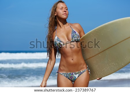 Hot surfer girl standing with surfboard on the beach, sexy bikini model with beautiful figure on summer travel vacation engage water sports, attractive woman in swimsuit holding her surfboard