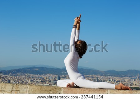 Yoga on high altitude with big city on background, woman stretching seated in yoga pose on amazing city background, woman meditating yoga and enjoying sunny evening, woman makes yoga on mountain hill
