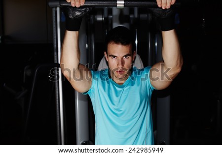 Muscular build man exercising on pulls up machine at gym