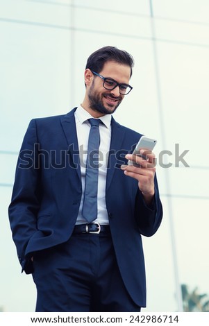 Happy businessman smiling as he reads a text message standing outside the office