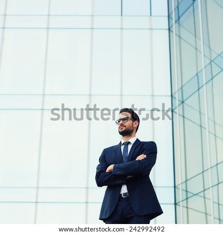 Upper half picture of handsome business man in glasses standing near skyscraper office building