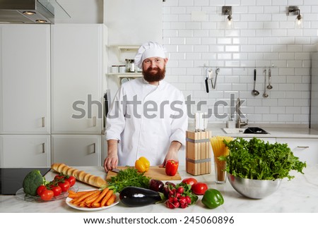 Portrait of a smiling male chef with fresh vegetables on big table standing in the kitchen