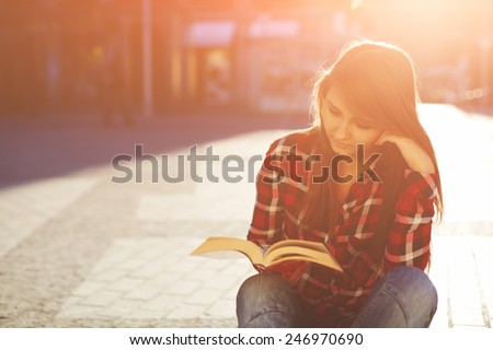 Portrait of a young hipster woman enjoying a good book sitting at sunny evening outdoors