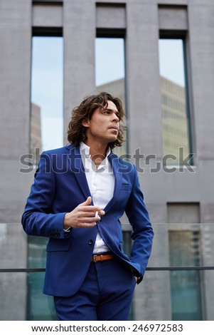 Attractive wealthy man in suit smoking cigarette looking into the distance while standing outdoors