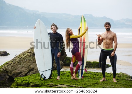 Group of young fancy people having fun while waiting surfing waves standing on the beach, surf camp holidays with international people