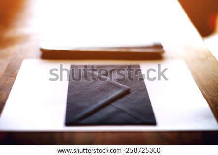 Close up with black envelope and digital tablet on wooden desk in home interior, mock up composition, filtered image, flare light, cross process,