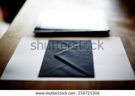 Close up with black envelope and digital tablet on wooden desk in home interior, mock-up composition